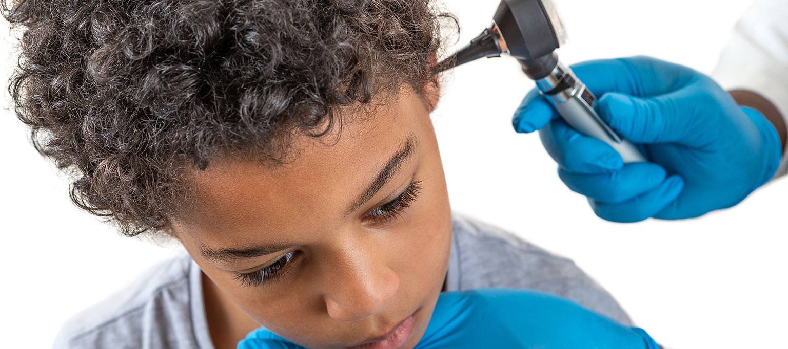 young boy with otoscope in ear by doctor