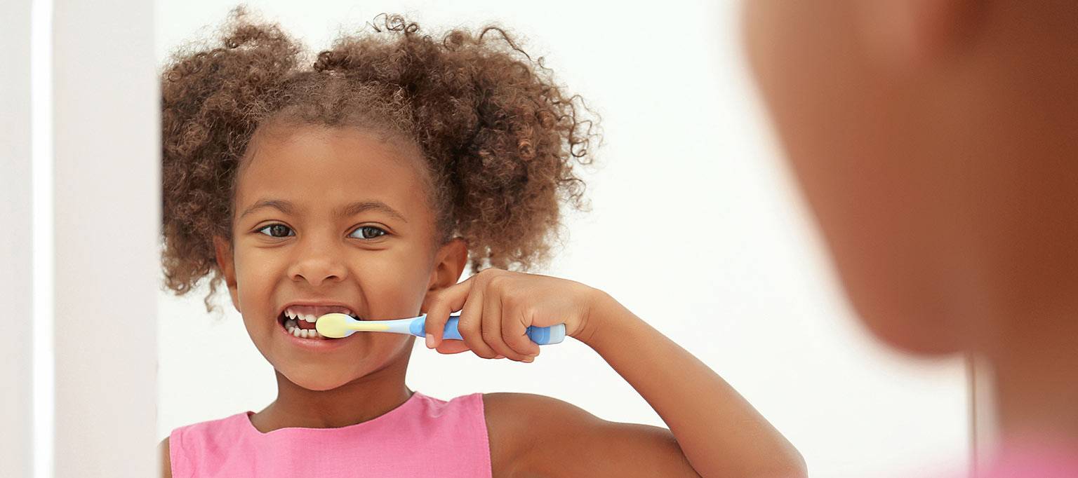 young girl cleaning teeth in front of mirror